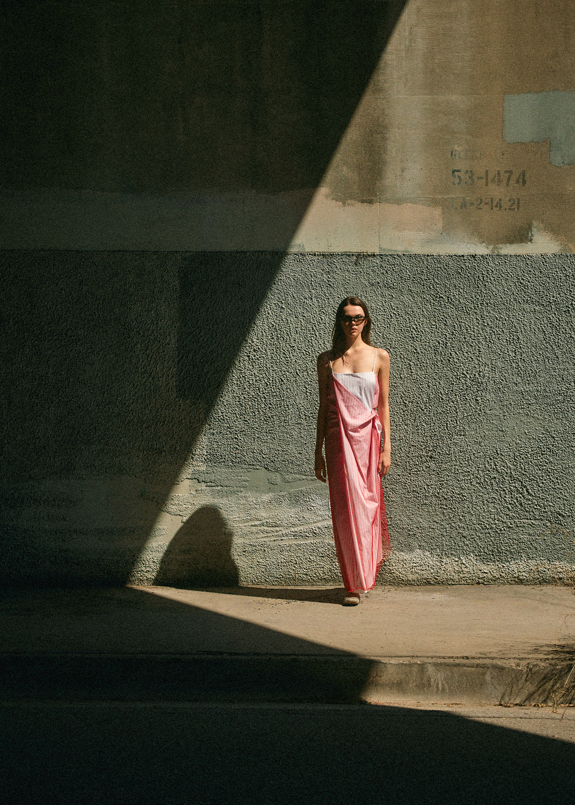 Caroline Cummings in a pink dress standing against a cement wall in the sunlight
